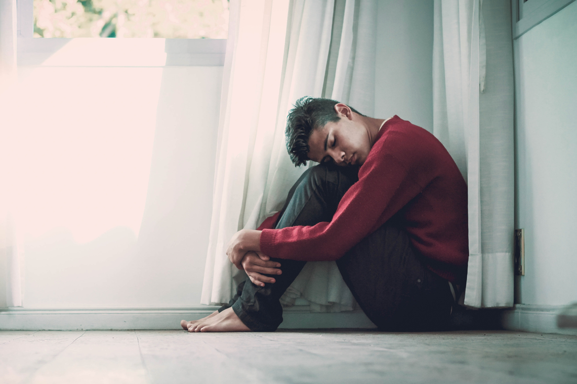 Young man sit on on the floor in a corner, head on knees.