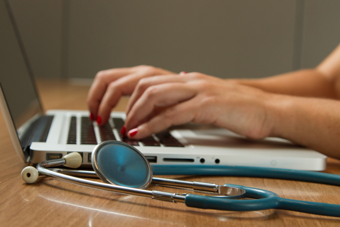 Two hand typing on laptop computer keyboard with stethoscope aside